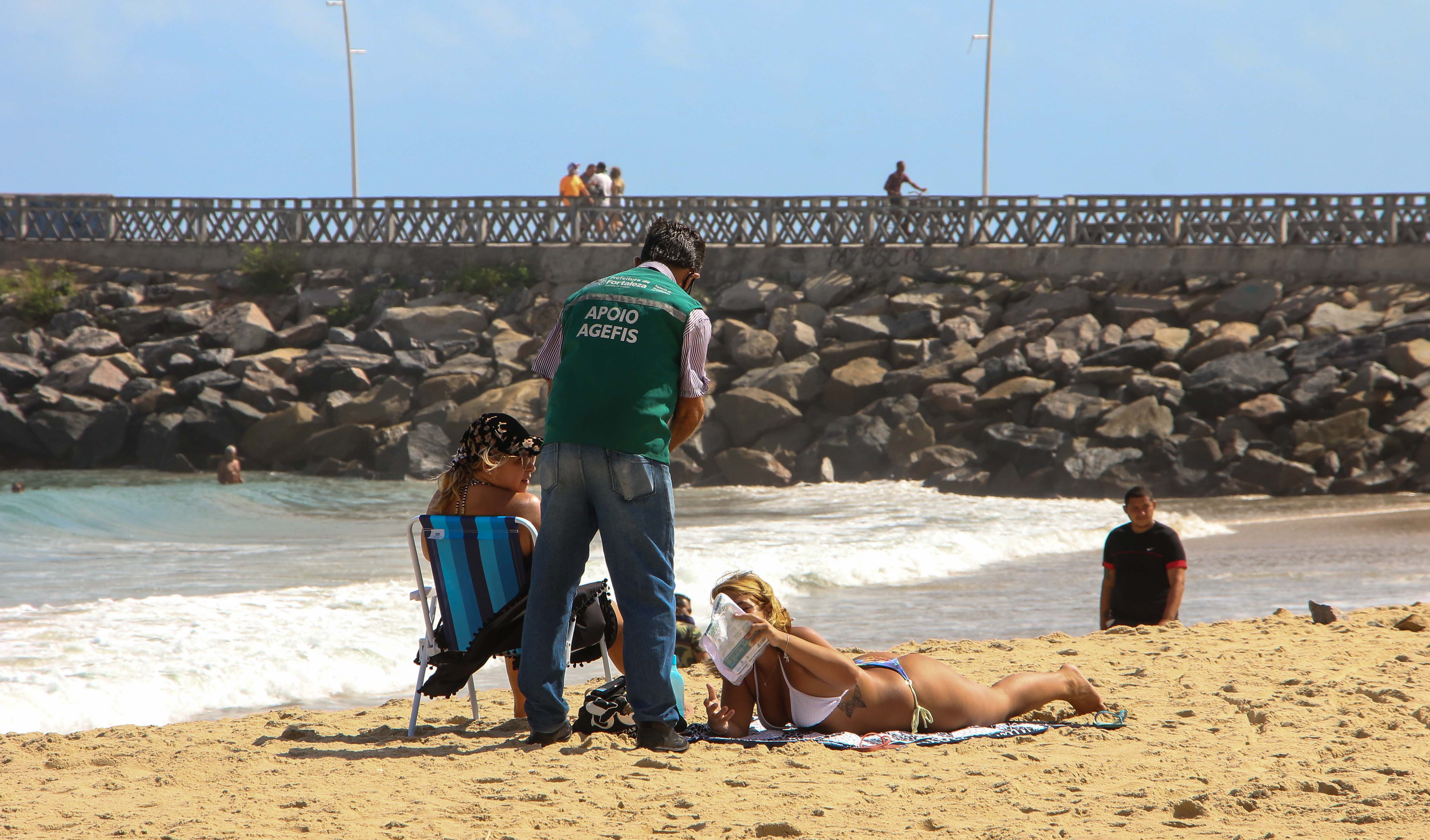 fiscais da Agefis em praia entregando kit para mulher deitada na areia de biquíni tomando sol